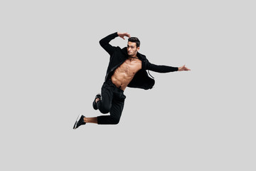 Wall Mural - Handsome young dancer of street dancing dressed in black pants and a sweatshirt on a naked torso jumps on a white background