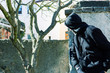 Unknown man in hood as robber or burglar or thief is spying around property with a plan to do illegal activity