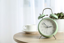 Beautiful Retro Alarm Clock With Cup Of Coffee And Succulent Plant On Table Against Light Background