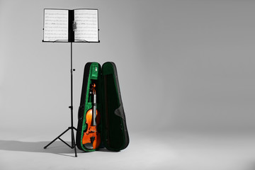 Wall Mural - Violin in case and note stand with music sheets on grey background. Space for text