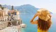 © zigres - Summer holiday in Italy. Back view of young woman holding her hat with Atrani village on the background, Amalfi Coast, Italy