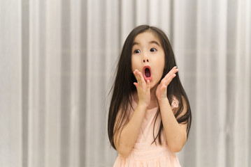 Surprising little cute Asian girl open her eyes and mouth so wide. She is feeling shock and surprise what she seeing. For sale advertisement concept.