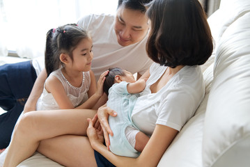 Happy family concept. Breast feeding newborn baby at home. The father and big sister stay close to mother and baby and looking at them, embracing and supporting her and the baby.