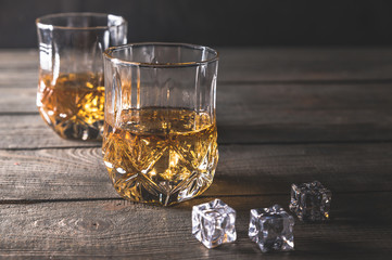 Two glasses of whiskey with ice cubes served on wooden planks 