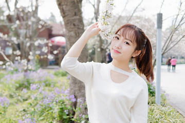 Outdoor portrait of beautiful young Chinese girl smiling among blossom cherry tree brunch in spring garden, beauty, summer, emotion, expression and people lifestyle concept.