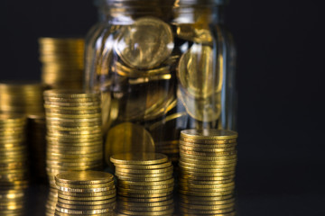 Coins stacks and gold coin money in the glass jar on dark background, for saving for the future banking finance concept.