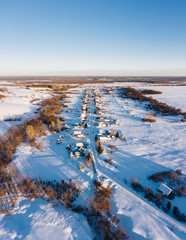 Wall Mural - Aerial view of a small village with the straight street and small houses surrounded by white winter fields and trees, a forest on the horizon, a clear blue sky at sunset. Penza oblast, Russia