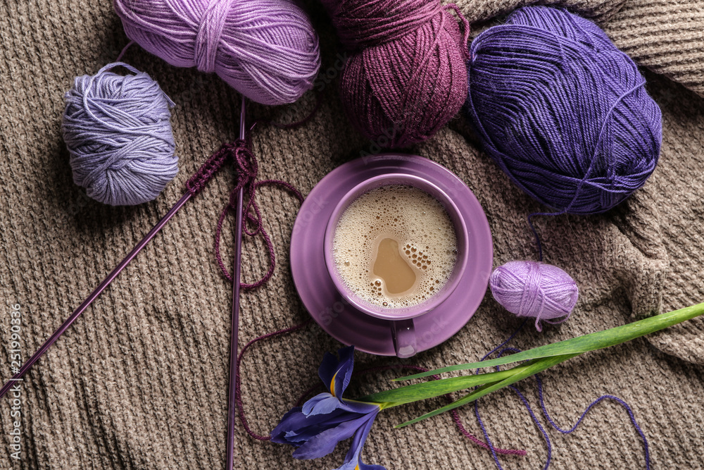 Cup of coffee with knitting yarn and flower on plaid