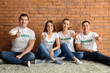 © Pixel-Shot - Team of young volunteers sitting near brick wall