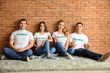 © Pixel-Shot - Team of young volunteers sitting near brick wall