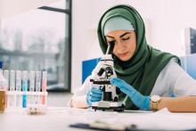 Beautiful Female Muslim Scientist Looking Through Microscope During Experiment In Chemical Laboratory