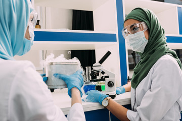 Wall Mural - female muslim scientists experimenting with microscope and dry ice in chemical laboratory