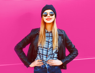 portrait cool blonde smiling girl in rock black style jacket, hat posing on city street over colorful pink wall background