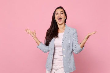 Portrait of cheerful excited young woman in striped jacket keeping mouth wide open, spreading hands isolated on pink pastel background. People sincere emotions, lifestyle concept. Mock up copy space.