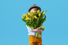 Cute Smiling Child Holding A Beautiful Bouquet Of Yellow Tulips In Front Of His Face Isolated On Blue. Little Toddler Boy Gives A Bouquet To Mom