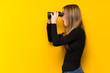 © luismolinero - Young pretty woman over yellow background and looking in the distance with binoculars