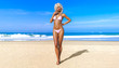 © vladnikon - 3D beautiful sun-tanned woman white swimsuit bikini on sea beach. Summer rest. Blue ocean background. Sunny day. Conceptual fashion art. Seductive candid pose. Realistic render illustration.