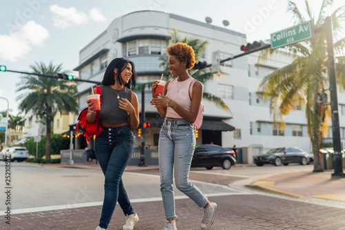 Fototapeta na szkło USA, Floryda, Miami Beach, dwie szczęśliwe koleżanki napijające się przez ulicę