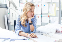 Pensive Woman Sitting At Desk In Office Surrounded By Paperwork