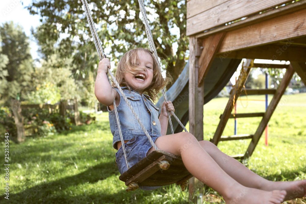 Laughing little girl sitting on swing in the garden Stock Photo | Adobe ...