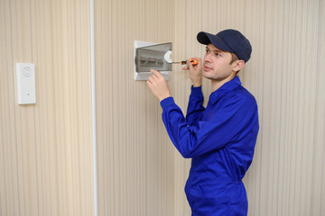 Wall Mural - lateral view of a young eletrician in blue overall disassembling a electrical panel with fuses in a house.