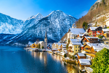 Classic postcard view of famous Hallstatt lakeside town in the Alps with traditional passenger ship on a beautiful cold sunny day with blue sky and clouds in winter, Salzkammergut region, Austria