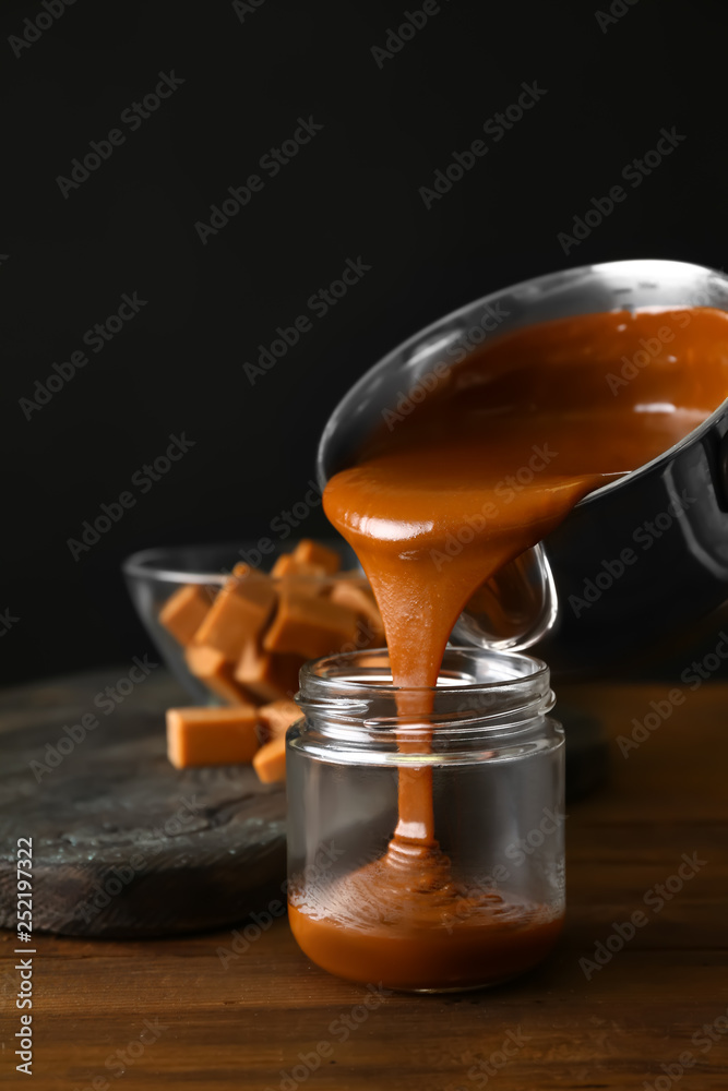 Liquid caramel pouring from pot into jar on table