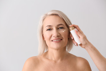 Wall Mural - Female hand applying serum onto mature woman's face against light background