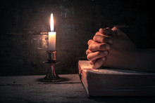 Close Up Hands Of Man Praying On Bible With Light Of Candle On Wooden Table At Worship Room. Christian Concept.