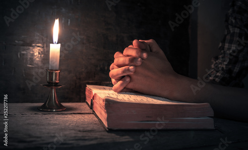 Close up hands of man praying on bible with light of candle. christian concept.
