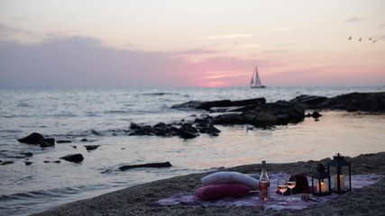 Wall Mural - Summer sea sunset. Romantic picnic on the beach. Bottle of wine, glasses, candles, plaid and pillows. Selective focus.