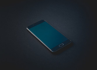 Dark-colored smartphone with the screen off lies on a black background