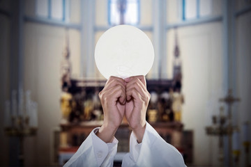 Hands of Priest raise a communion bread in church