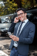 © Viktoriia - Leisure time. Businessman in eyeglasses wearing earphones leaning on wall on the city street listening song browsing playlist on smartphone happy