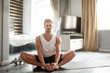 © estradaanton - Young well-built man go in for sports in apartment. Calm and peaceful guy hold hands on feet and stretch legs. Young man's eyes are closed.