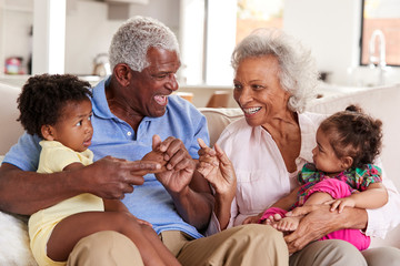 Wall Mural - Grandparents Sitting On Sofa At Home Playing With Baby Granddaughters