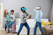 © alfa27 - Multiethnic diverse friends enjoying VR technology, two guys wearing vr headset and playing while african and caucasian redhead girl look at them and laugh. Futuristic Gadget concept