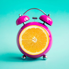 Summer time concepts with orange alarm clock on blue pastel background.