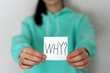 WHY and question mark on a white piece of paper in the hands of a teenager
