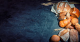 Fototapeta Tulipany - Assortment of fresh baked bread on dark background. White and rye bread, buns with copy place