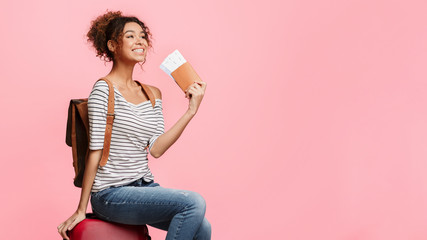 African-american woman with passport sitting on suitcase