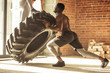Young muscular woman flipping a tire on hard training with personal trainer at the garage gym.
