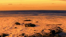Orange Ocean Under Orange Sky Sunset With Waves Hitting Rocks And Creating Beautiful Foam