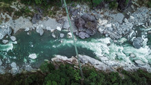 Suspension Bridge Over Rio Cangrejal River In Pico Bonito National Park. Top Down Aerial Drone View. High Up. Tourists On Bridge Over Rushing River. Moody Low Light With Dark Colors.