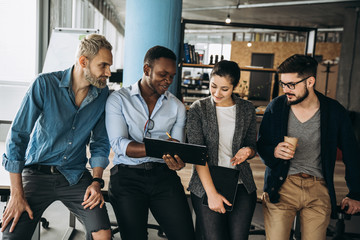 Wall Mural - Group of young modern people in smart casual wear smiling and discussing something while working in the creative office