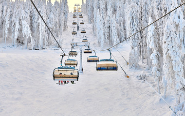 Chair lift in Poiana Brasov ski resort, Skiers and snowboarders enjoy the ski slopes in Poiana Brasov winter resort whit forest covered in snow on winter season