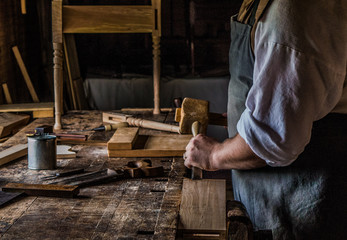 Carpenter working with equipment on wooden chair in his carpentry shop