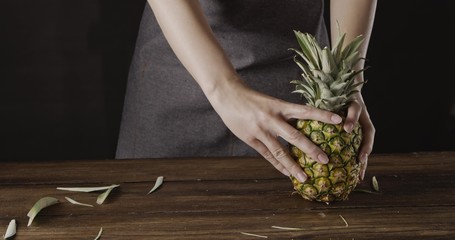 Wall Mural - Woman' hands with ripe juicy natural organic tropical fruit pineapple on a wooden kitchen table on a black background.