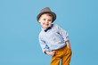 Portrait of happy joyful  little boy isolated on blue background. Toddler child in hat and fashionable suit smiling and have a fun 