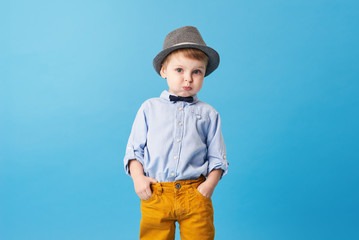 Wall Mural - Portrait of happy joyful  little boy isolated on blue background. Toddler child in hat and fashionable suit smiling and have a fun. Copy space for text right side